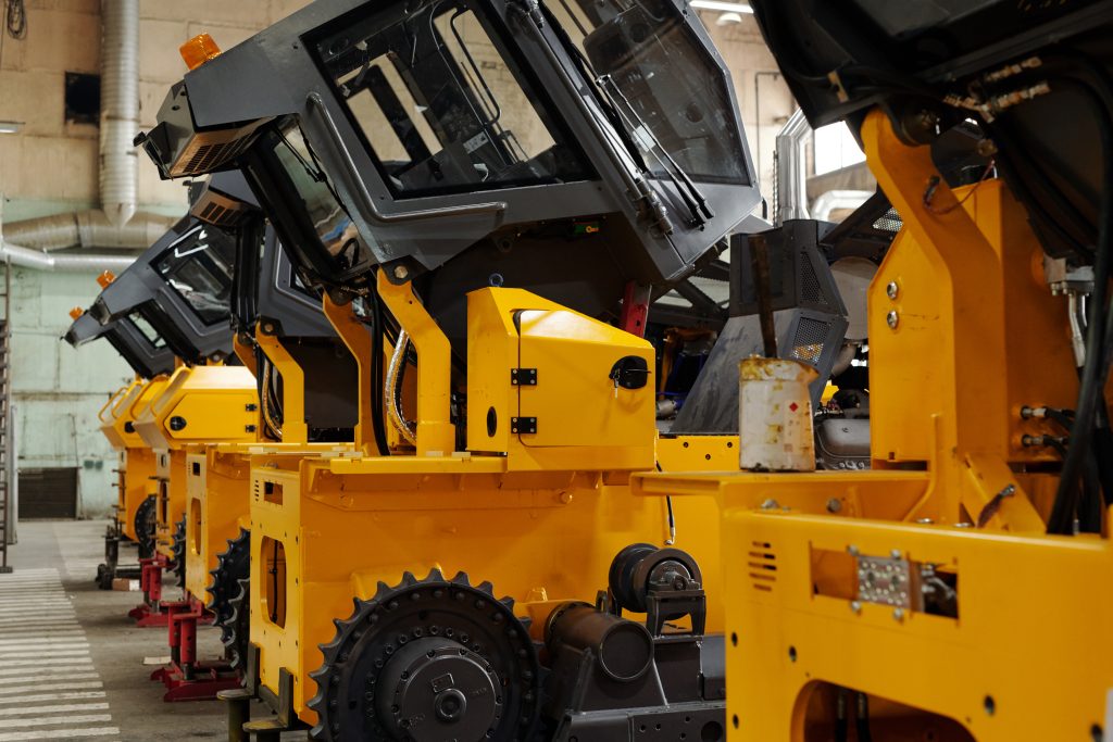 Perspective of several huge industrial machines of yellow color standing in row in large warehouse or workshop of modern plant